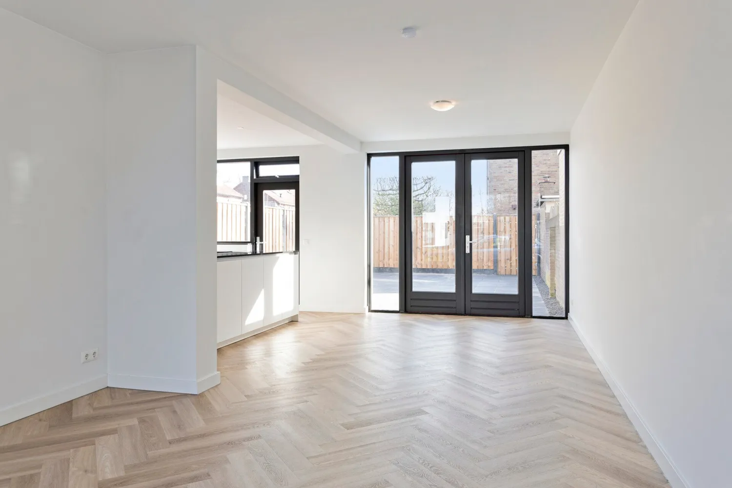 Woonkamer na de renovatie: visgraatvloer, strak stucwerk en stalen deuren